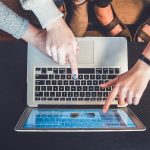 Young people pointing at a certain element on the screen of a laptop.